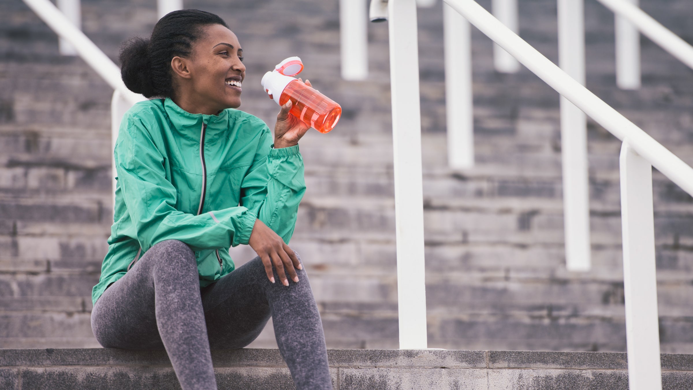 Women in sports clothing drinking water, sitting on stadium stairs.