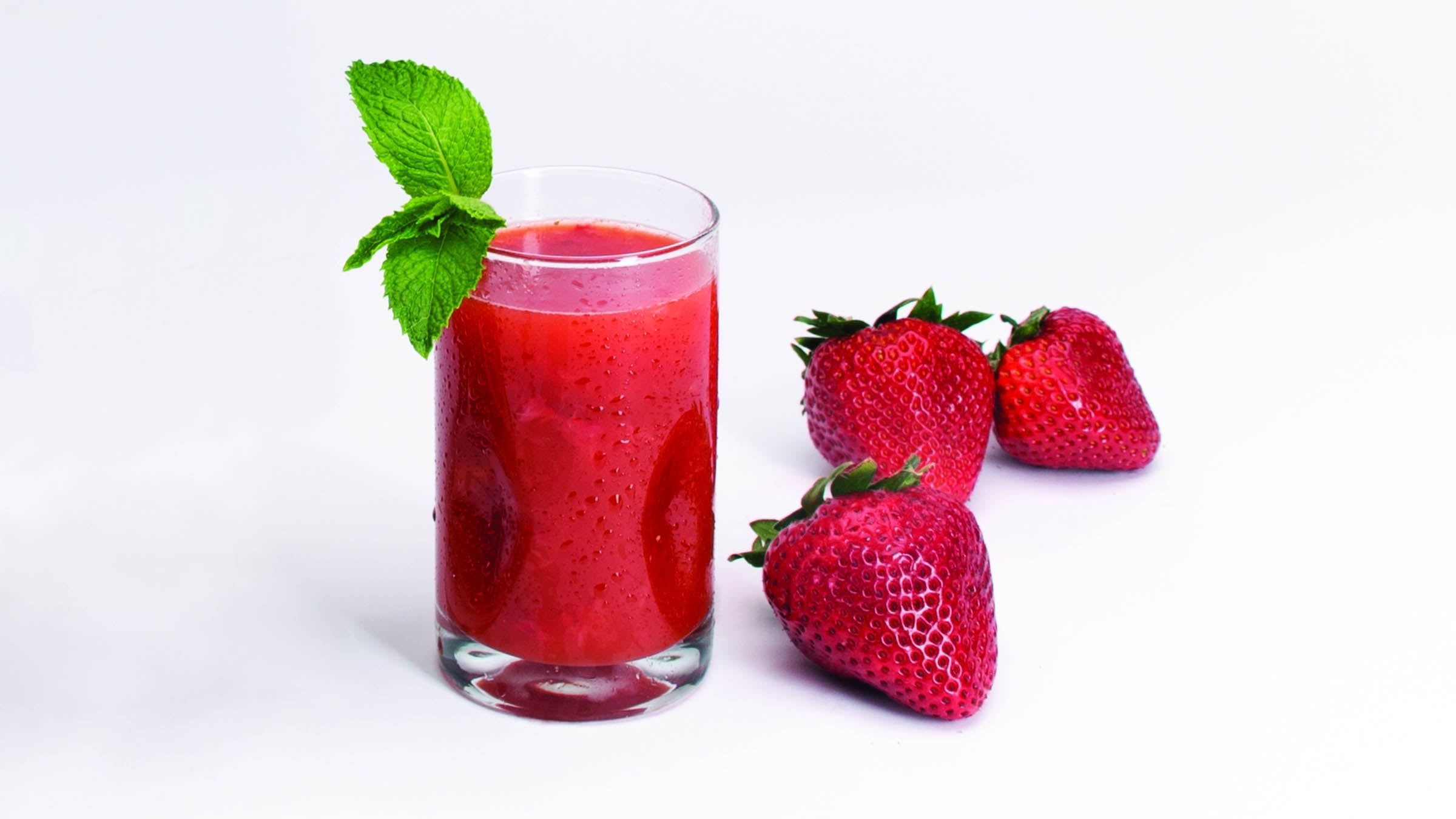 Beachy bloody mary in a tall glass with mint garnish, next to a few strawberries