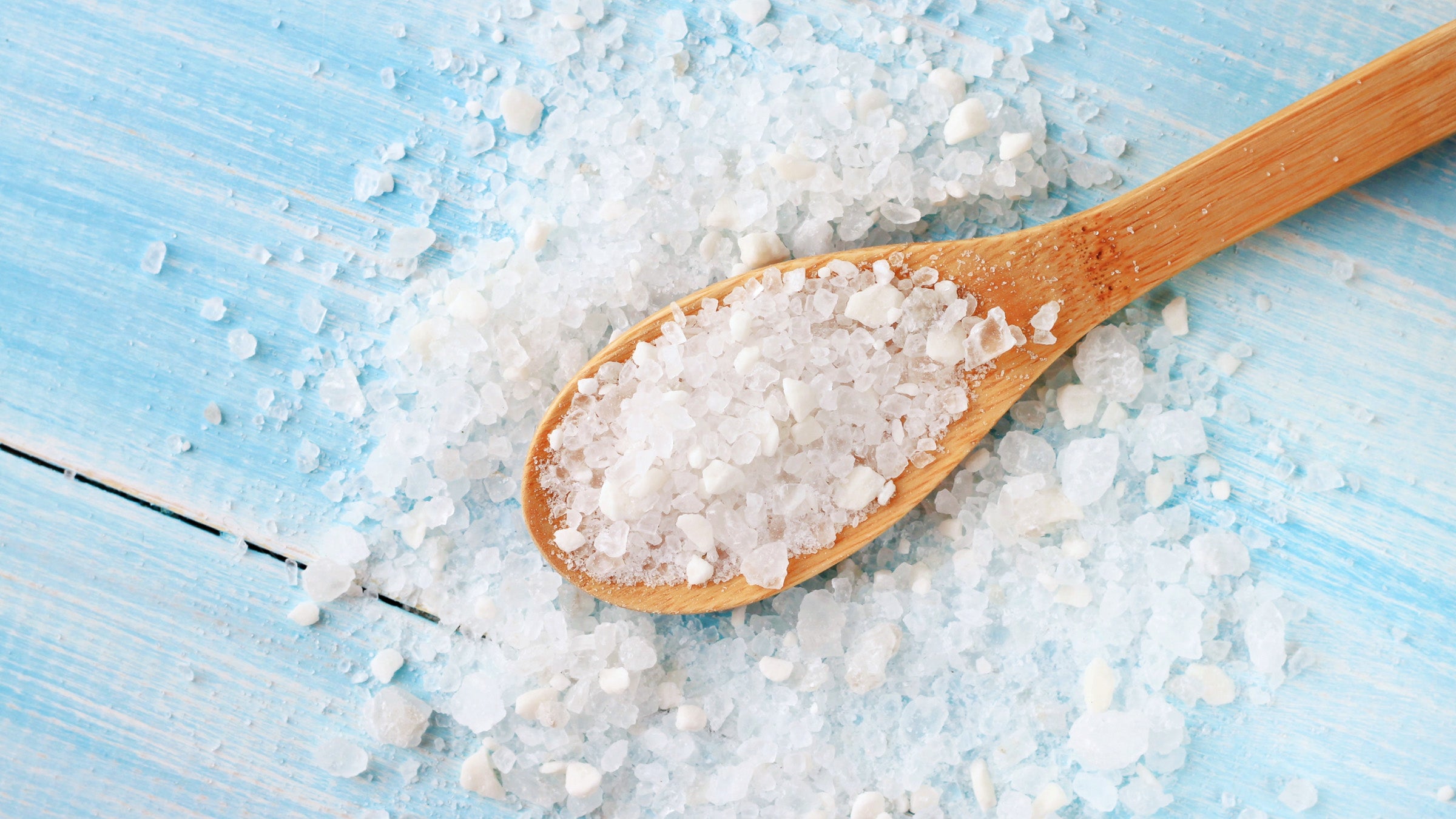 Large grains of sea salt in a wooden spoon on blue table