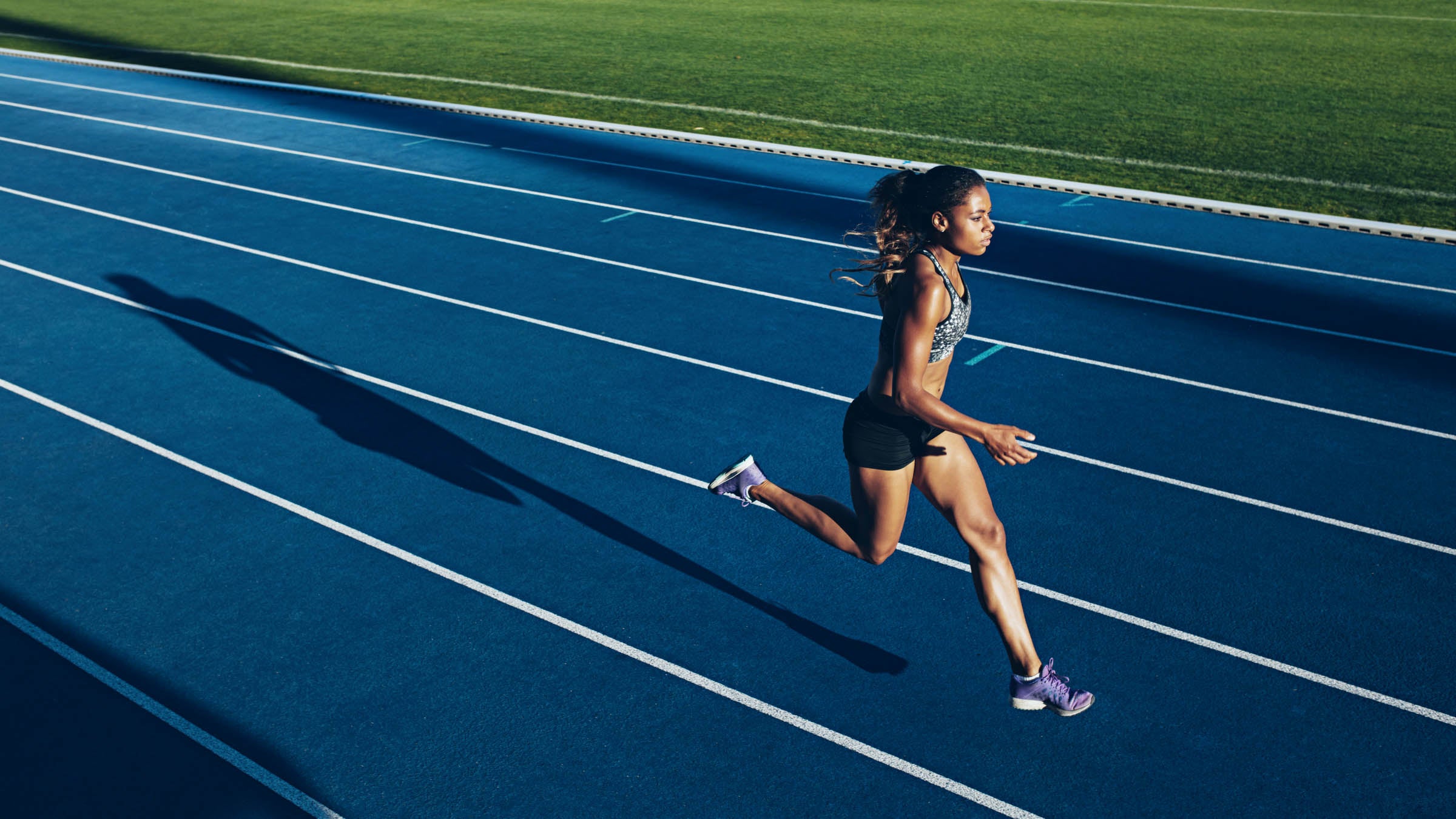 Outdoor shot of young female athlete running on racetrack.