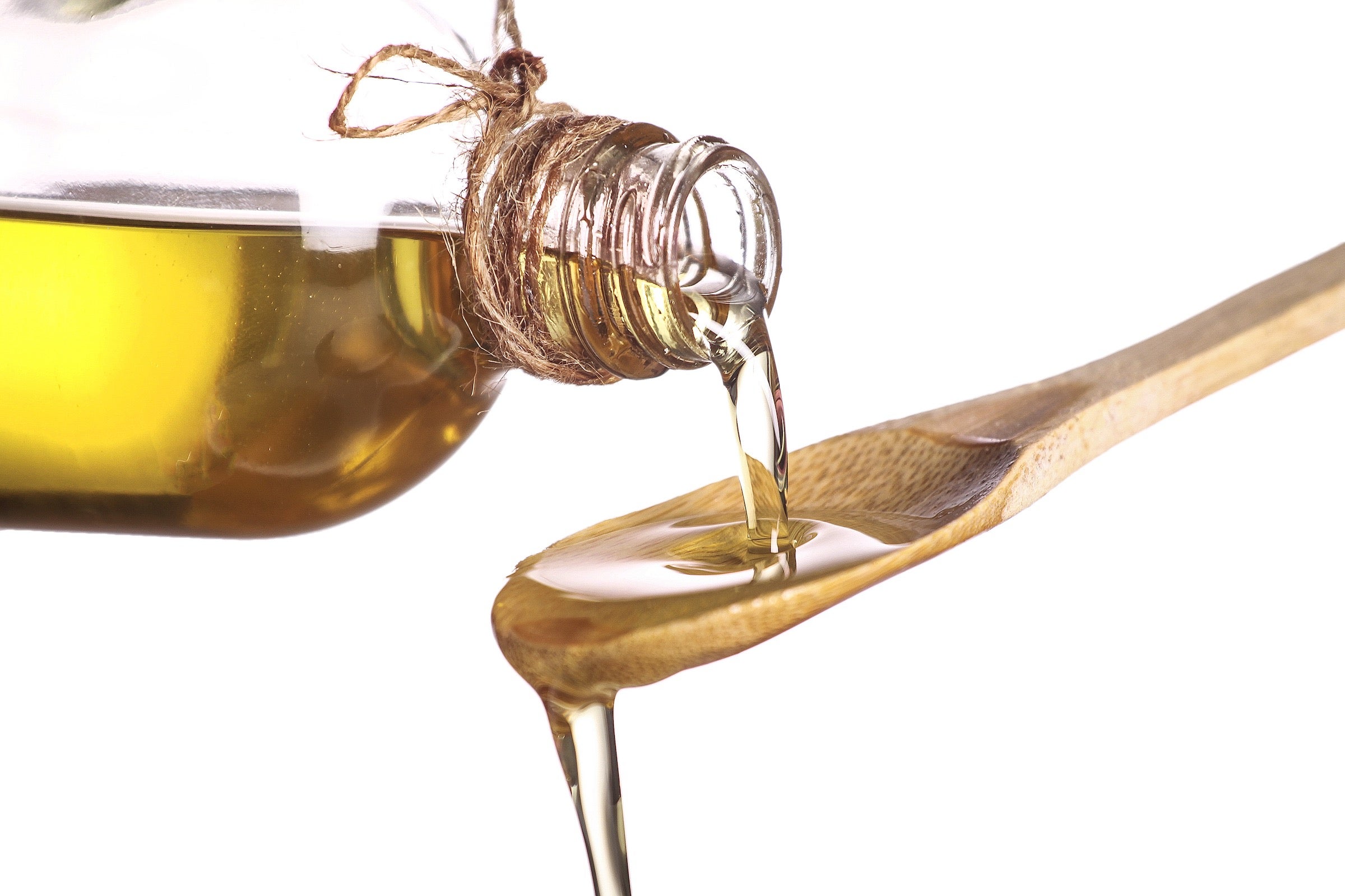 close-up of pouring olive oil, a plant-based fat, on spoon isolated on white background