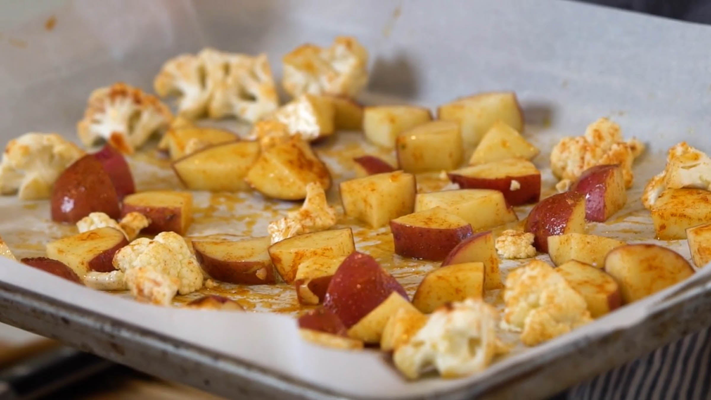 Sliced potatoes and cauliflower seasoned and on a baking sheet