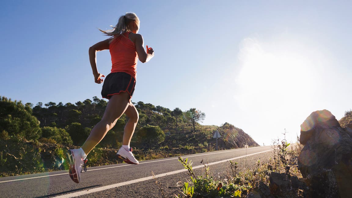 Blonde woman in pink top and old school Nike shoes running on an uphill road.