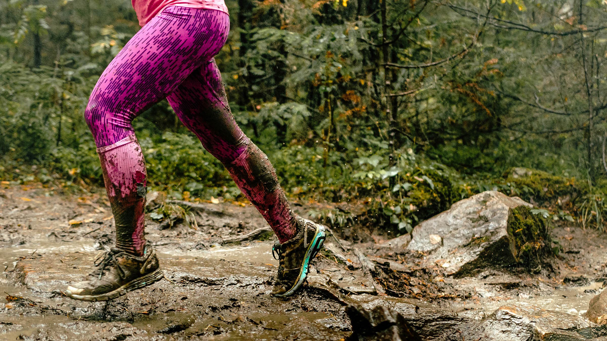 Lower shot of woman running over muddy rocks in forest