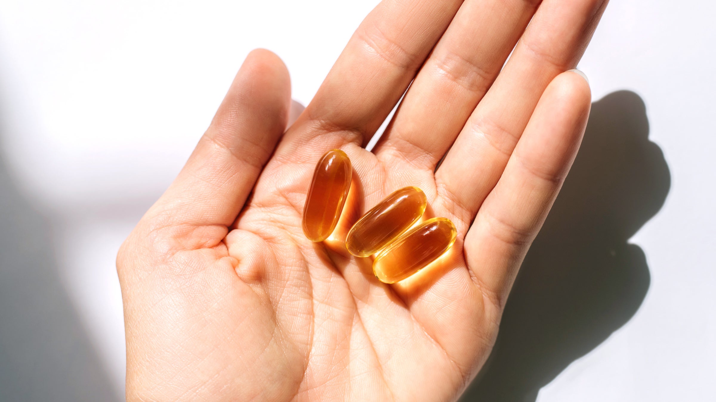 Woman's hand holding supplements on white background.