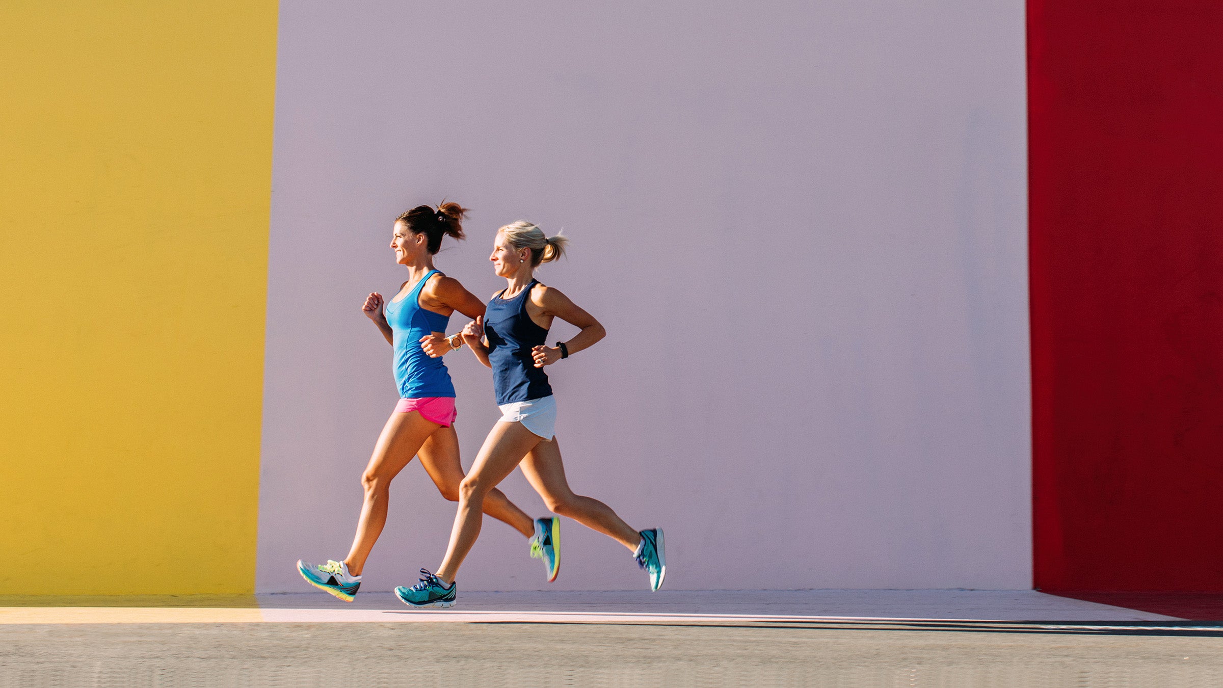 Two women and friends are running against a color wall in the city
