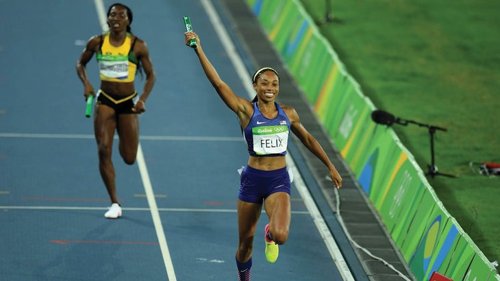 Allyson Felix holds her relay baton aloft while crossing the finish line