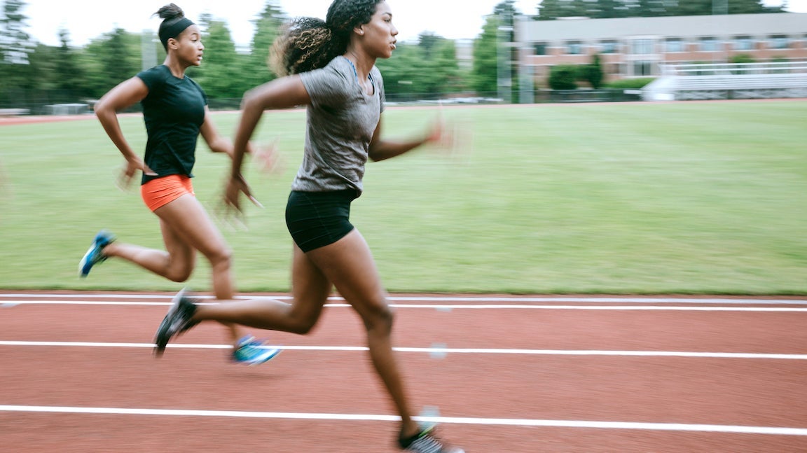 Young adult women sprint down the track, their motion intentionally blurred to show their speed. Training for track and field competition.