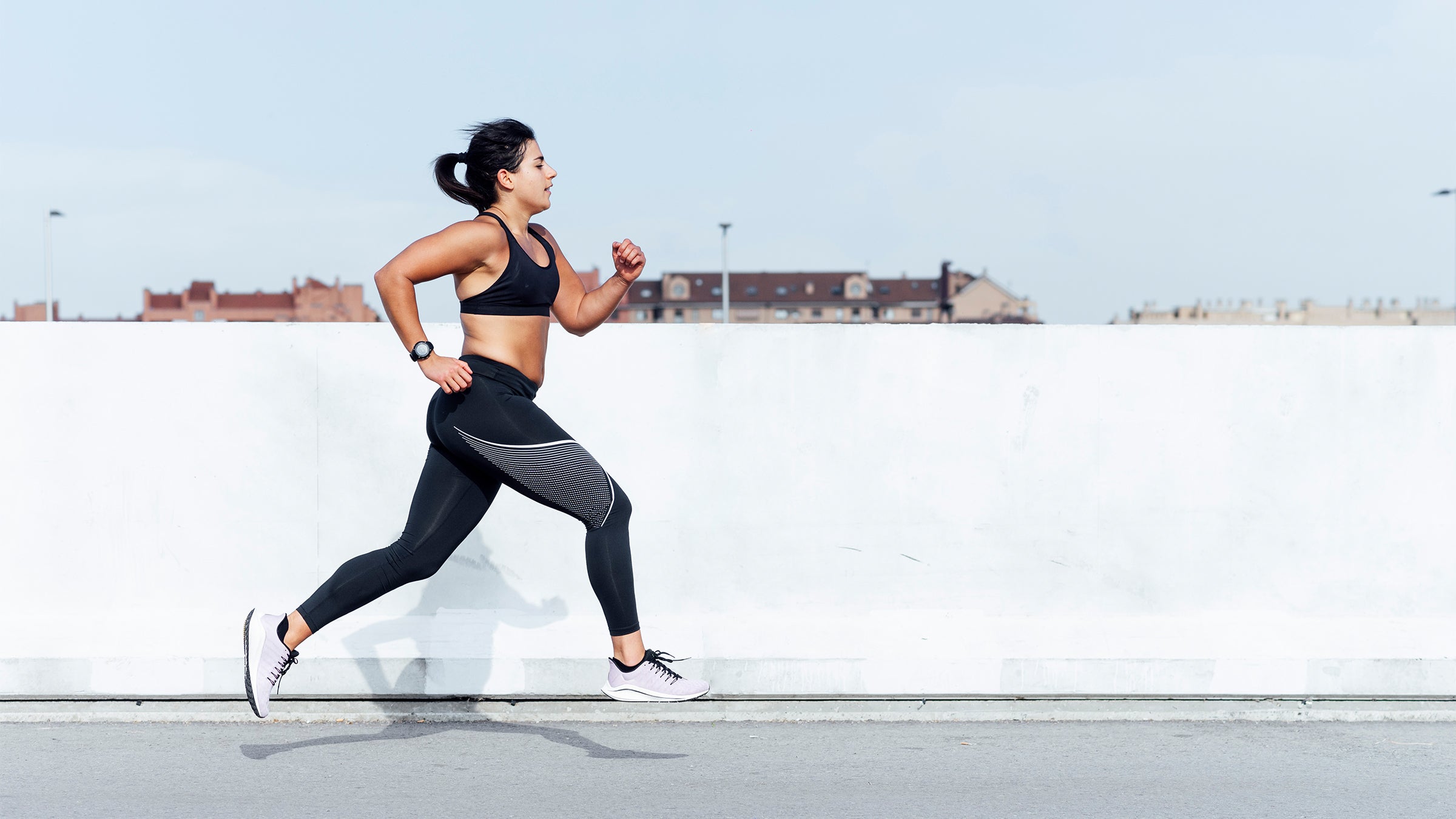 Woman in a black running outfit against a white wall
