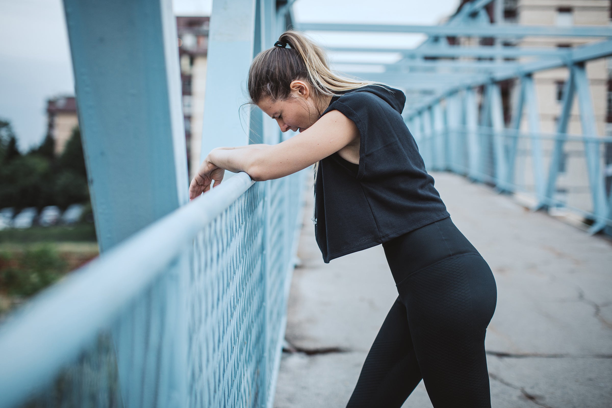 female runner trying to decide if she should quit running on bridge