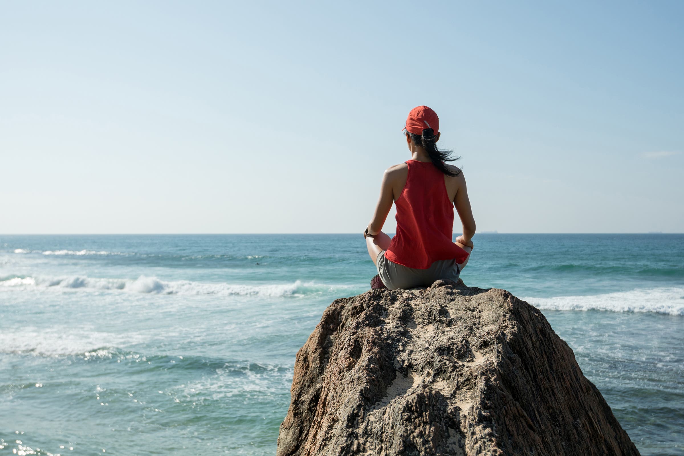 female runner practicing meditation on seaside rock