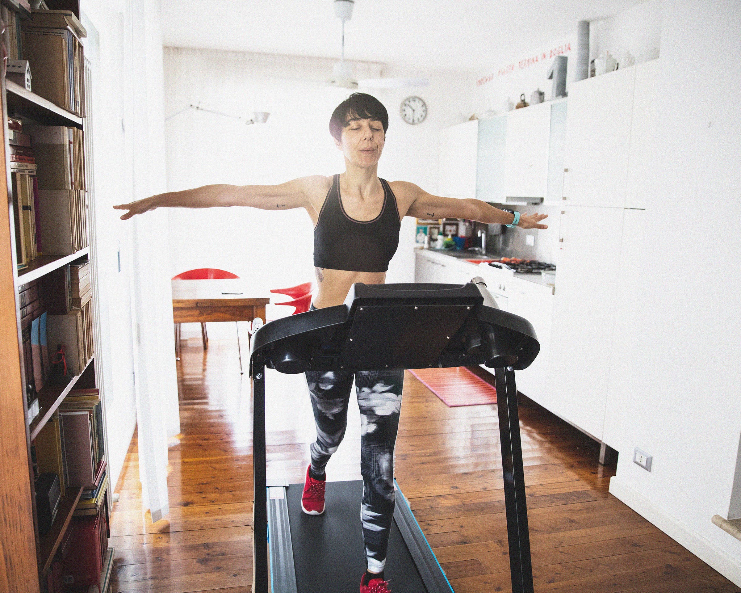 woman spreading her arms while running on a treadmill at home