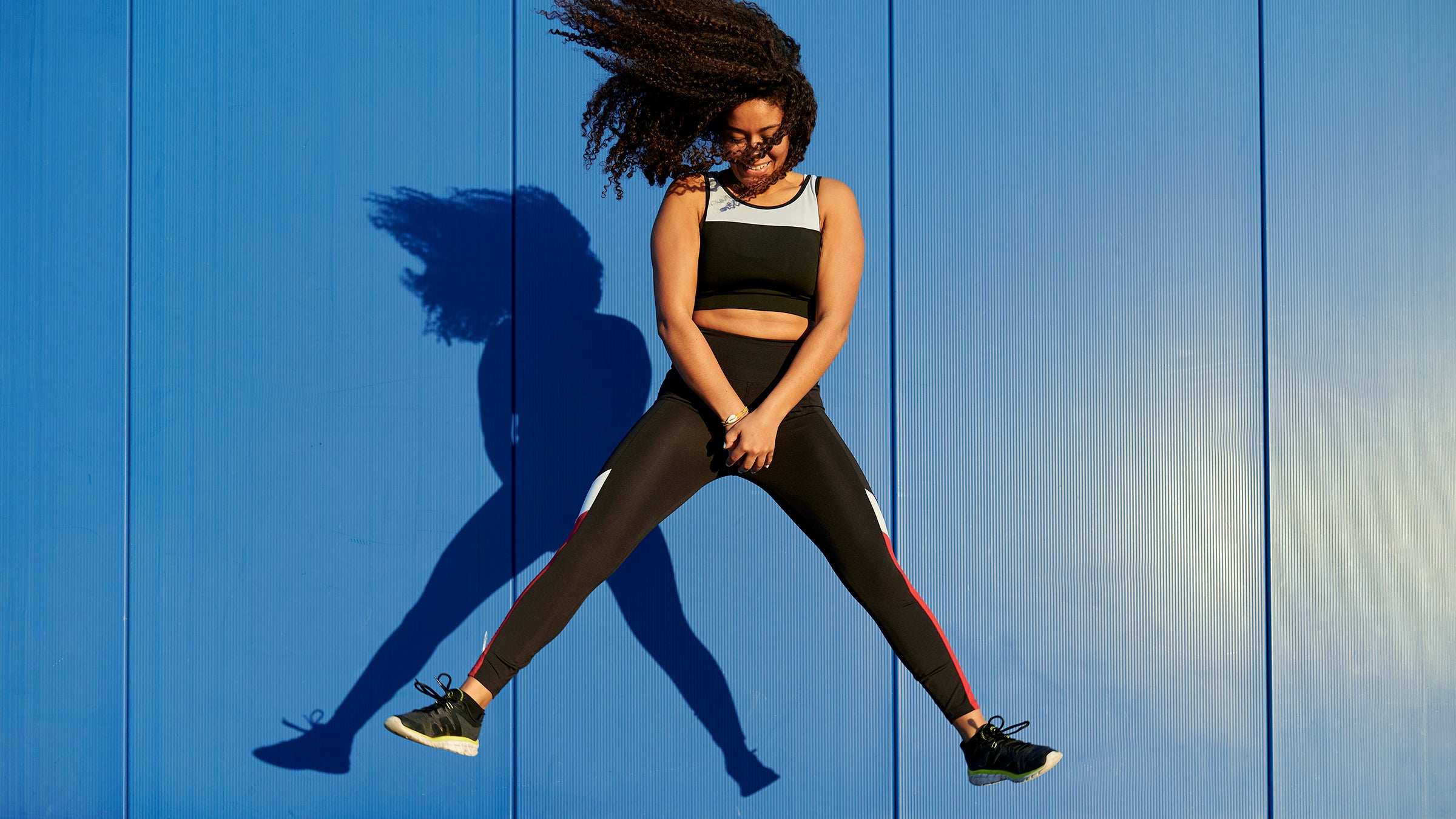 Sportswoman with legs apart jumping in front of blue wall, representing a link between running and UTIs