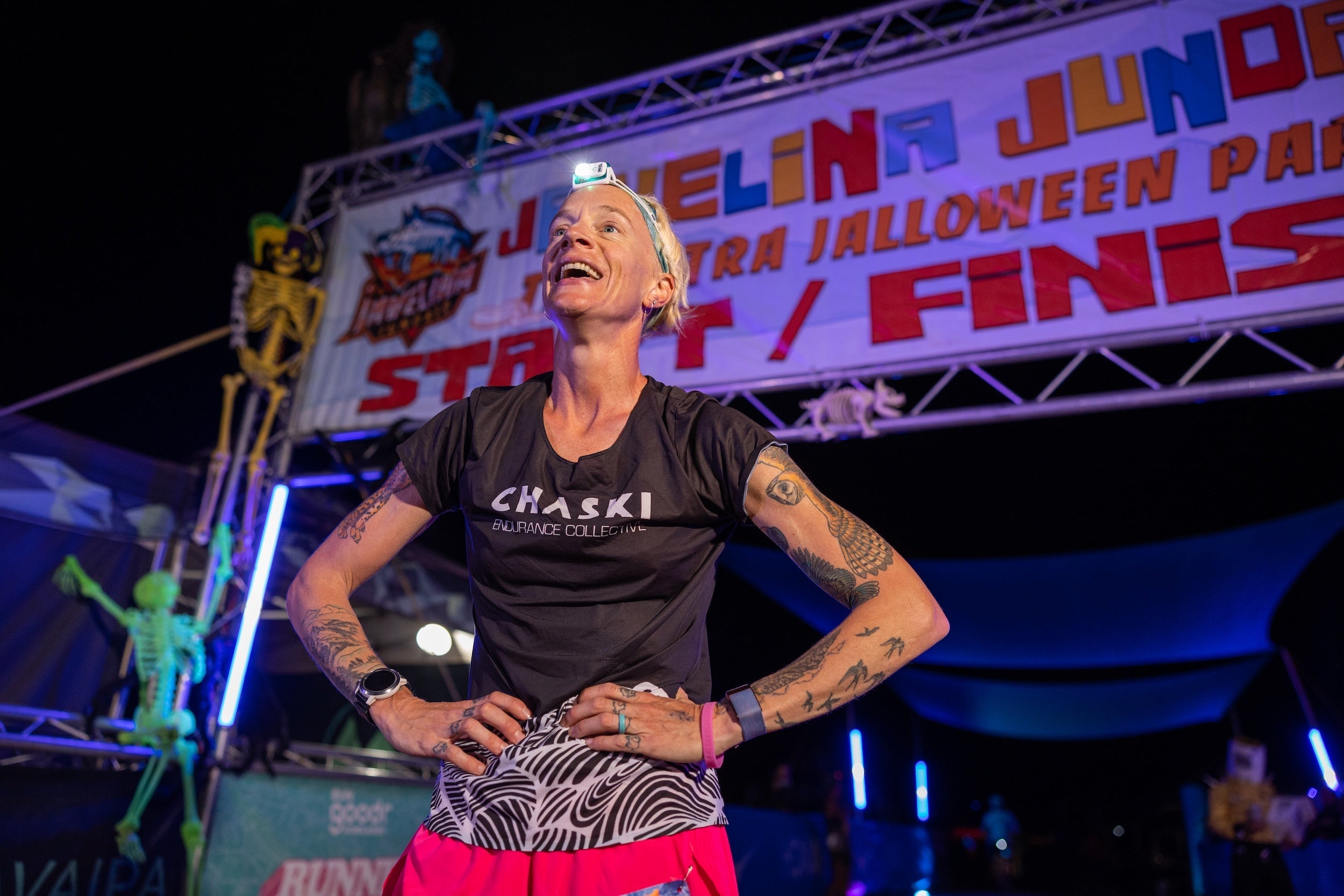 woman at the finish line of a 100-mile race at night with a black shirt and headlamp
