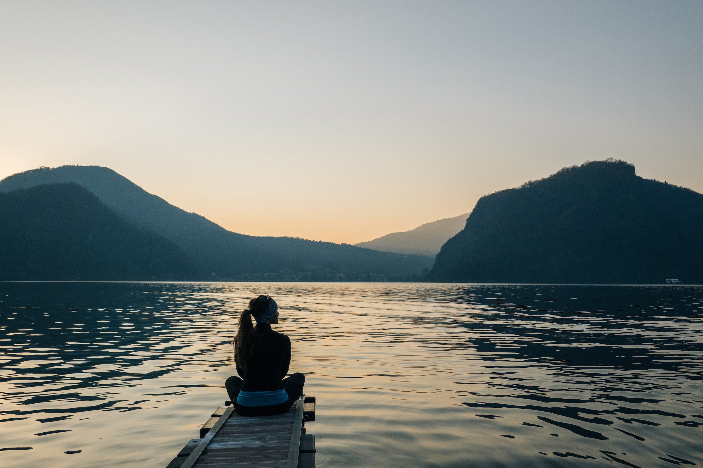 Woman sit spotting on a small dock at a mountainous lake